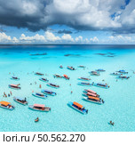 Aerial view of colorful boats in transparent water on sunny day. Mnemba island, Zanzibar. Top view of sandbank in low tide, blue sea, sand, swimming people, yachts, sky with clouds in summer. Ocean. Стоковое фото, агентство Ingram Publishing / Фотобанк Лори