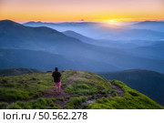 Man on the top of mountain Goverla, Ukraine. Hill with green grass and beautiful mountain valley at sunset in summer. Landscape with sporty man, hils in fog, orange sky. Hiking. Spring in Europe. Стоковое фото, агентство Ingram Publishing / Фотобанк Лори