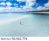Aerial view of alone young woman on the sandbank in ocean, white sand, blue sea during low tide at sunny summer day in Zanzibar island. Top view of girl, sand spit, bay, clear water, sky with clouds. Стоковое фото, агентство Ingram Publishing / Фотобанк Лори