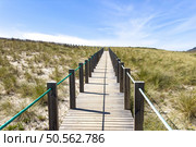 A wooden boardwalk through sand dunes leads to a coastal town of Vila Praia de Ancora nestled against hills. Стоковое фото, агентство Ingram Publishing / Фотобанк Лори