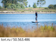 A man enjoys a peaceful ride on an electric hydrofoil surfboard near a tranquil shoreline, blending adventure with calm nature. Стоковое фото, агентство Ingram Publishing / Фотобанк Лори