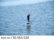 Hydrofoiling on a calm blue sea, a person showcases balance and skill, gliding effortlessly on the water surface under a sunny sky. Стоковое фото, агентство Ingram Publishing / Фотобанк Лори