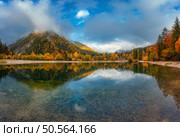 Mountain lake reflecting colorful trees with red and orange foliage at autumn sunset. Dramatic landscape with water, foggy forest, mountains in low clouds in fall. Jasna lake, Kranjska Gora, Slovenia. Стоковое фото, агентство Ingram Publishing / Фотобанк Лори