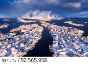 Aerial view of snowy Henningsvaer fishing village, Lofoten islands, Norway in winter at sunset. Top drone view of mountains in snow, sea, boats, bridge, road, cloudy sky, town, rorbuer and houses. Стоковое фото, агентство Ingram Publishing / Фотобанк Лори