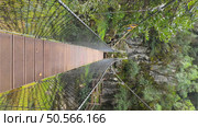 Suspended footbridge spanning a mossy gorge connects hiking trails through limestone cliffs, featuring wooden planks and safety cables in a lush natural setting. Rio de Mouros pathway in Condeixa, Coimbra Portugal. Стоковое фото, агентство Ingram Publishing / Фотобанк Лори