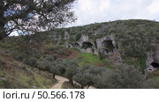Buracas do Casmilo at Condeixa - Portugal. Ancient limestone caves nestled in a rugged hillside, featuring multiple natural cavern openings amid green vegetation and moss-covered rock formations on a cloudy day. Стоковое фото, агентство Ingram Publishing / Фотобанк Лори