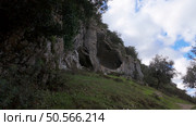 Buracas do Casmilo at Condeixa - Portugal. Ancient limestone caves nestled in a rugged hillside, featuring multiple natural cavern openings amid green vegetation and moss-covered rock formations on a cloudy day. Стоковое фото, агентство Ingram Publishing / Фотобанк Лори