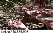 Pink picnic table in a shaded outdoor setting with flowers and dappled light during the afternoon. Стоковое AI-изображение, AI-художник Сергей Толмачёв / Фотобанк Лори