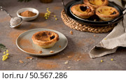 Pastel de Nata on a plate with cinnamon sprinkled around, surrounded by a sieve, a bowl of cinnamon, and more tarts on a woven mat. Стоковое фото, агентство Ingram Publishing / Фотобанк Лори
