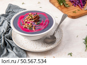 Purple cabbage soup with a vibrant pink swirl, garnished with chopped pecans and fresh rosemary, served in a speckled white bowl on a matching plate. Стоковое фото, агентство Ingram Publishing / Фотобанк Лори