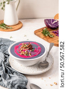 Purple cabbage soup garnished with pecans and rosemary, served in a white bowl on a speckled plate, with a spoon and a cutting board with herbs and cabbage in the background. Стоковое фото, агентство Ingram Publishing / Фотобанк Лори