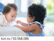 A small girl stood at the foot of the bed playing with the younger sibling carried by his mother and smiling with affection, In a bedroom surrounded by warmth and family. Стоковое фото, агентство Ingram Publishing / Фотобанк Лори