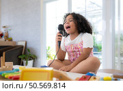 A tiny girl sits on a toy table, clutching a microphone, and sings cheerfully in the living room. Стоковое фото, агентство Ingram Publishing / Фотобанк Лори