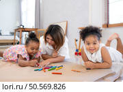On a holiday, A woman and her two little daughters sit on the floor and drawing together in the living room. Стоковое фото, агентство Ingram Publishing / Фотобанк Лори