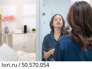Asian young woman in a blue pajama is brushing her teeth in front of the mirror before taking a shower. Стоковое фото, агентство Ingram Publishing / Фотобанк Лори
