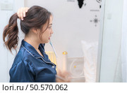 Asian young woman in a blue pajama is brushing her teeth in front of the mirror before taking a shower. Стоковое фото, агентство Ingram Publishing / Фотобанк Лори