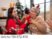 A little granddaughter lovingly hugs her grandmother, while they eating a meal together during the Christmas celebration at home. Стоковое фото, агентство Ingram Publishing / Фотобанк Лори