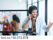 Portrait of smiling businessman talking on mobile phone while colleague using scooter in office. Стоковое фото, агентство Ingram Publishing / Фотобанк Лори