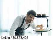 A young man puts on an apron to make dessert to eat with his wife. Checking the completeness of the finished dessert. Стоковое фото, агентство Ingram Publishing / Фотобанк Лори