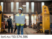 Portrait of railway technician worker in safety vest and helmet working with blueprint at train repair station. Стоковое фото, агентство Ingram Publishing / Фотобанк Лори