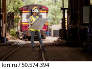 Portrait of railway technician worker in safety vest and helmet working with blueprint at train repair station. Стоковое фото, агентство Ingram Publishing / Фотобанк Лори