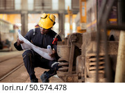 Railway technician in uniform and helmet inspect the train wheels removed from the locomotives in the train workshop. Стоковое фото, агентство Ingram Publishing / Фотобанк Лори