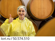 Smiling female winemaker in yellow uniform standing in cellar of winery. Стоковое фото, агентство Ingram Publishing / Фотобанк Лори