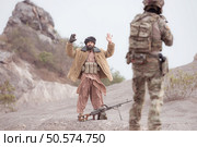 A Taliban soldier stands with a machine gun, Raise hands in surrender to the allied soldiers, In the desert mountain terrain battlefield. Стоковое фото, агентство Ingram Publishing / Фотобанк Лори