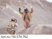 A Taliban soldier stands with a machine gun, Raise hands in surrender to the allied soldiers, In the desert mountain terrain battlefield. Стоковое фото, агентство Ingram Publishing / Фотобанк Лори