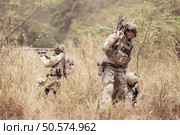 Soldiers in camouflage military uniforms carrying weapons, Reconnaissance missions in the tropical forest area with mission of helping those injured from being shot. Стоковое фото, агентство Ingram Publishing / Фотобанк Лори