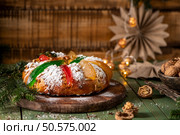 Festive holiday bread adorned with colorful candied fruits and dusted with powdered sugar, set on a rustic wooden board with Christmas decorations in the background. Стоковое фото, агентство Ingram Publishing / Фотобанк Лори