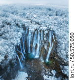 Aerial drone view of amazing waterfall and snowy forest at sunset. Winter fairytale in Plitvice Lakes, Croatia. Top view of white snow-covered frozen trees, waterfall, house, clouds on cold winter day. Стоковое фото, агентство Ingram Publishing / Фотобанк Лори
