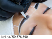 Permanent make-up for eyebrows of beautiful woman with thick brows in beauty salon. Closeup beautician doing  tattooing eyebrow. Стоковое фото, агентство Ingram Publishing / Фотобанк Лори