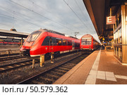 Beautiful railway station with modern red commuter train at colorful sunset in Nuremberg, Germany. Railroad with vintage toning. Стоковое фото, агентство Ingram Publishing / Фотобанк Лори