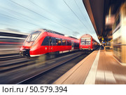 Modern high speed red passenger commuter trains at the railway platform at sunset. Railway station in Nuremberg, Germany. Railroad with motion blur effect. Industrial concept landscape. Transportation. Стоковое фото, агентство Ingram Publishing / Фотобанк Лори
