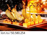 Closeup image of canapes with cheese, grapes, apple slices at wooden table with falling snow background. Стоковое фото, агентство Ingram Publishing / Фотобанк Лори
