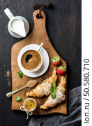 Breakfast set. Two freshly baked croissants with strawberries, honey, cup of black coffee, pitcher with milk and spoon with brown sugar on rustic wooden board over dark background, top view, vertical composition. Breakfast set. Two freshly baked croissants with strawberries, honey, cup of black coffee, pitcher and spoon on rustic wooden board over dark background. Стоковое фото, агентство Ingram Publishing / Фотобанк Лори