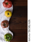 Top view of heirloom tomatoes on a kitchen towel and dark wood table. Стоковое фото, агентство Ingram Publishing / Фотобанк Лори