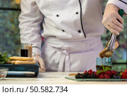 Hand with tongs holding biscuit. Glass with dark liquid. Chef dips savoiardi into coffee. Mastery of confectioner.. Hand with tongs holding biscuit. Стоковое фото, агентство Ingram Publishing / Фотобанк Лори