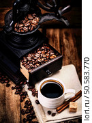 Cup of coffee with coffee beans and Coffee grinder on wooden brown background closeup.  Espresso Cup on brown napkin with cinnamon sticks  and sugar.. Cup of coffee with coffee beans and Coffee grinder on wooden brown background closeup.  Espresso Cup on brown napkin with cinnamon . Стоковое фото, агентство Ingram Publishing / Фотобанк Лори