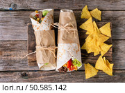 Mexican style dinner. Two papered tortillas burrito with beef and vegetables served with nachos chips over old wooden background. Flat lay. Tortillas and nachos. Стоковое фото, агентство Ingram Publishing / Фотобанк Лори