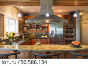 Breakfast bar in contemporary upscale home kitchen interior with granite countertops, accent lighting and stainless steel appliances including vent hood and refrigerator. Стоковое фото, агентство Ingram Publishing / Фотобанк Лори