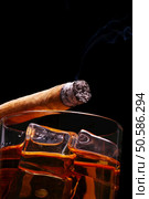 Lit Cigar resting on Glass of Whiskey and Ice cubes with wisp of smoke and black background, low angle. Стоковое фото, агентство Ingram Publishing / Фотобанк Лори