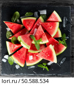 Organic seedless watermelon cut into wedges with ice and mint  on a slate board over black background, top view. Стоковое фото, агентство Ingram Publishing / Фотобанк Лори