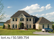 Very large and beautiful stone and brick house on a small lake with generic car in front circle drive and white puffy clouds in the sky. Стоковое фото, агентство Ingram Publishing / Фотобанк Лори