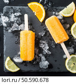 Homemade orange popsicles with ice and citrus fruits on stone black background. Summer food concept. Top view.. Homemade orange popsicles. Стоковое фото, агентство Ingram Publishing / Фотобанк Лори