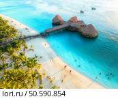 Aerial view of beautiful bungalow in Indian ocean at sunset in summer. Restaurant on the sea. Top view of wooden hotel, palm trees, azure water, white sandy beach. Luxury resort in Kendwa, Zanzibar. Стоковое фото, агентство Ingram Publishing / Фотобанк Лори