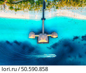 Aerial view of bungalow, boat in Indian Ocean at sunset in summer. Restaurant on the sea. Top drone view of wooden hotel, azure water, white sandy beach, palm trees. Luxury resort in Kendwa, Zanzibar. Стоковое фото, агентство Ingram Publishing / Фотобанк Лори