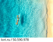 Aerial view of young woman lying on transparent canoe in blue sea at sunset. Summer in Zanzibar. Top drone view of beautiful slim girl, kanoe, sandy beach, ocean with clear water. Tropical background. Стоковое фото, агентство Ingram Publishing / Фотобанк Лори