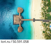 Aerial view of bungalow, white sandy beach, ocean on summer sunny day. Restaurant on the sea. Top drone view of wooden hotel, azure water, green palms. Luxury resort in Kendwa, Zanzibar. Tropical. Стоковое фото, агентство Ingram Publishing / Фотобанк Лори
